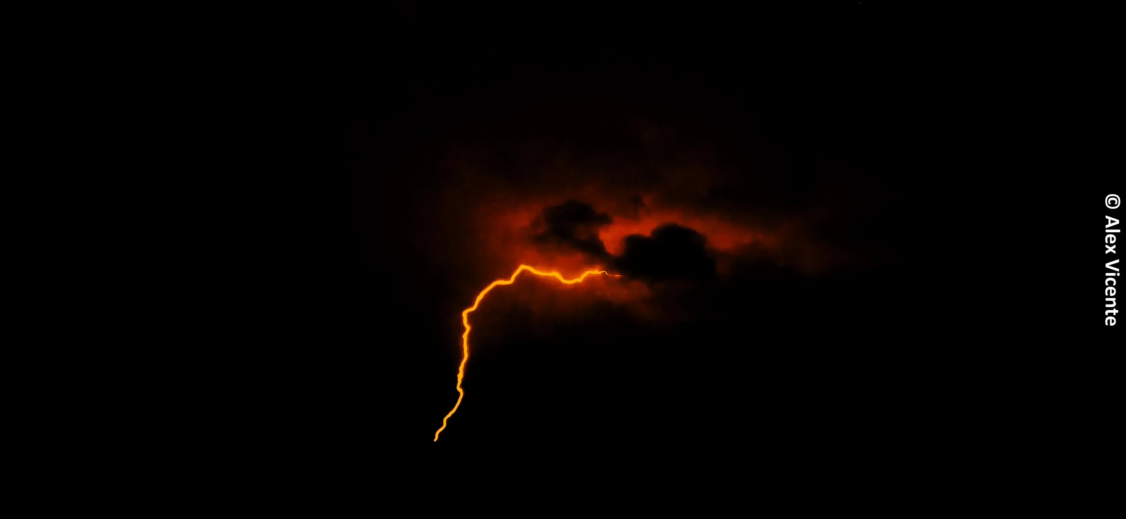 Lightning crossing glowing storm clouds at dusk.