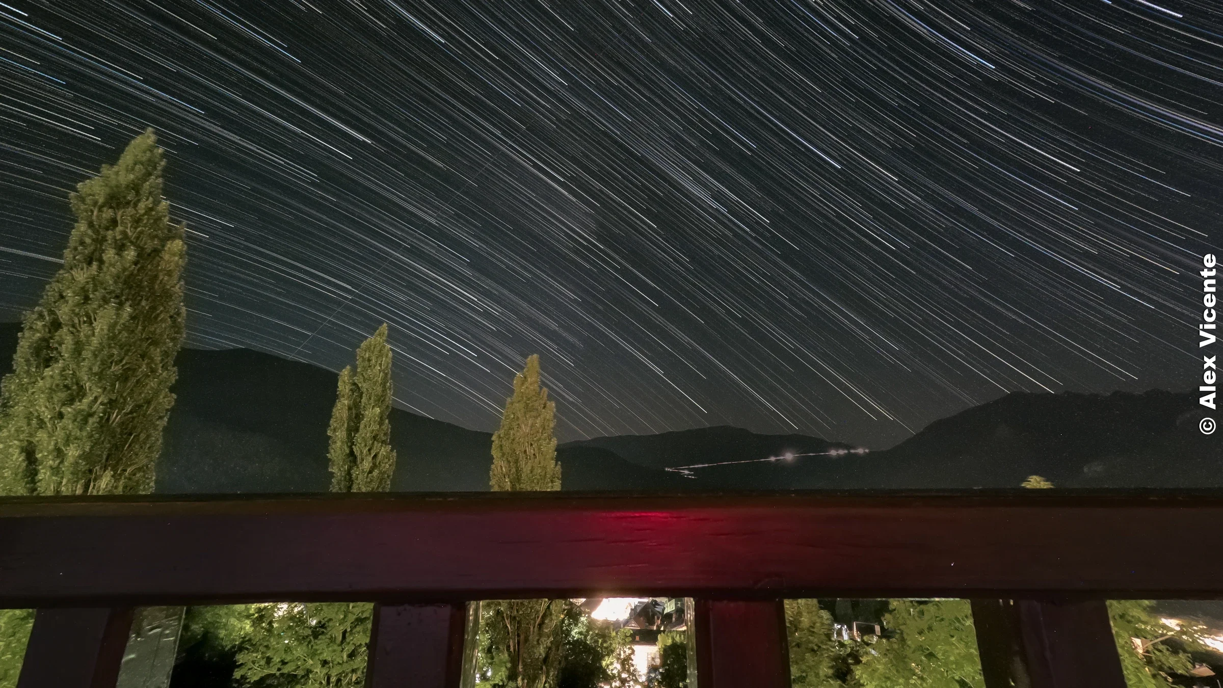 Star trails crossing the night sky above a mountain valley.